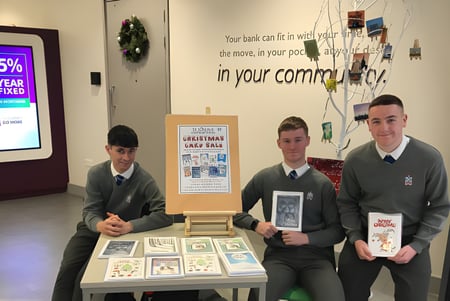 Tres estudiantes en uniforme están detrás de una mesa de exhibición con varios objetos en el campus de la St. Joseph's Secondary School.