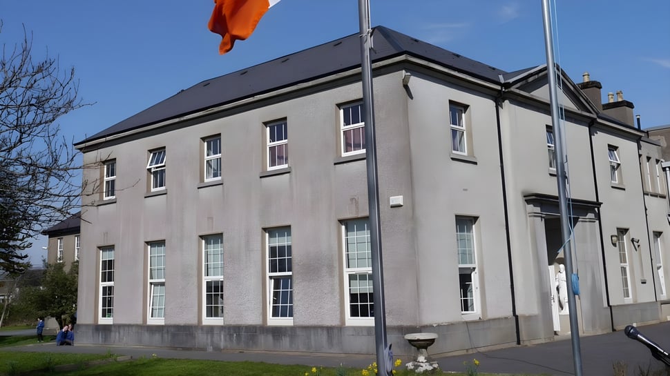El edificio de varios pisos de la St. Joseph’s Secondary School en Castlebar con una bandera naranja frente a un cielo azul.