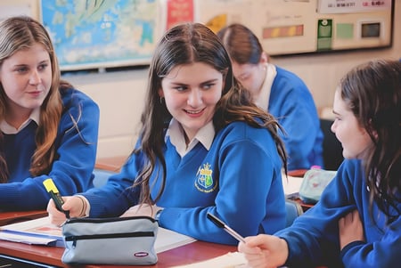 Estudiantes de la St. Joseph’s Secondary School están sentados juntos en una mesa y trabajan en el aula.