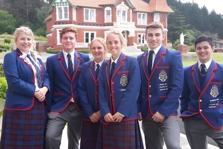 Estudiantes en uniformes escolares posan frente al gran edificio rojo y blanco en el terreno de St. Kevin’s College.