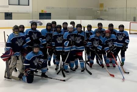 Un grupo de jugadores de hockey de St. Kevin's High School posan juntos en una pista de hielo frente a una portería.