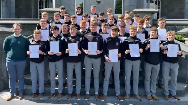 Un grupo de estudiantes de St. Kieran’s College está frente a un edificio académico y sostiene orgullosamente sus certificados.