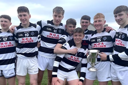 Un grupo de estudiantes de St. Kieran’s College está con un trofeo deportivo en un campo de césped bajo un cielo nublado.