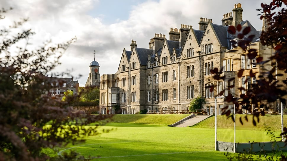 El histórico edificio de la St. Leonards School se encuentra en medio de un césped verde con árboles y un cielo nublado.