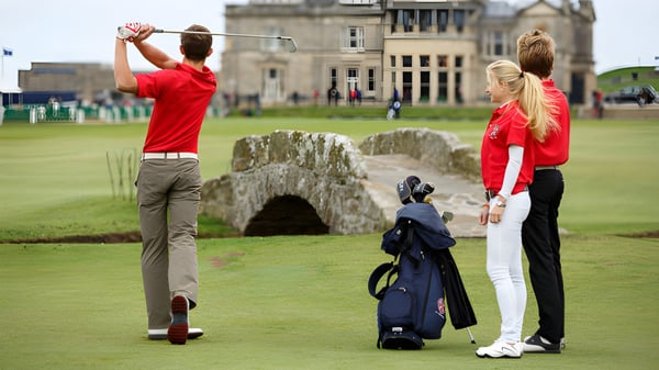 Dos estudiantes de la St. Leonards School juegan al golf en un césped frente a un histórico edificio de piedra.