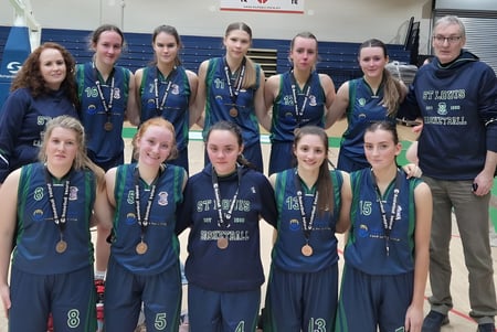 Un grupo de jóvenes atletas en uniforme deportivo posan frente a una cancha de baloncesto en el campus de la St. Louis Secondary School.