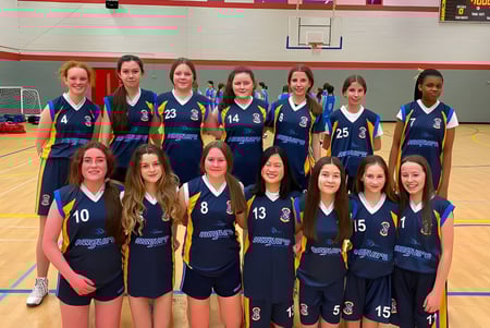 Un grupo de jóvenes jugadoras de baloncesto en camisetas azul oscuro posan en la cancha de baloncesto de la St. Louis Secondary School.