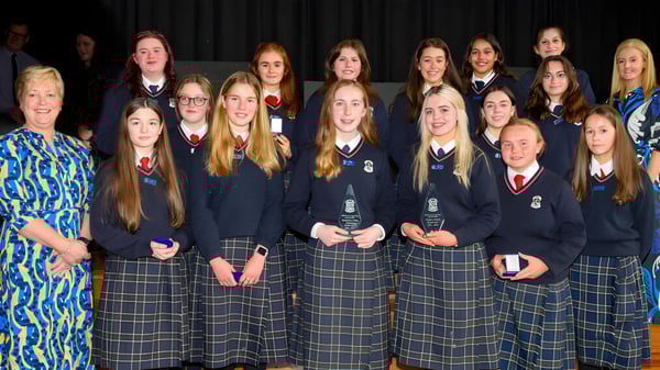 Un grupo de estudiantes de la St. Louis Secondary School posan juntos frente a una cortina oscura.