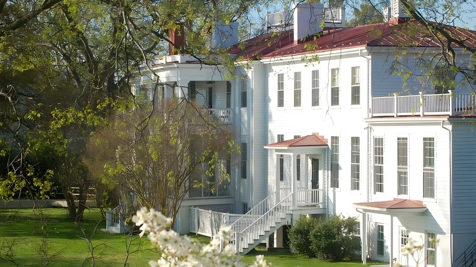 El edificio blanco de St. Margaret's School con techo rojo está rodeado de árboles verdes y una pradera bien cuidada en primer plano.