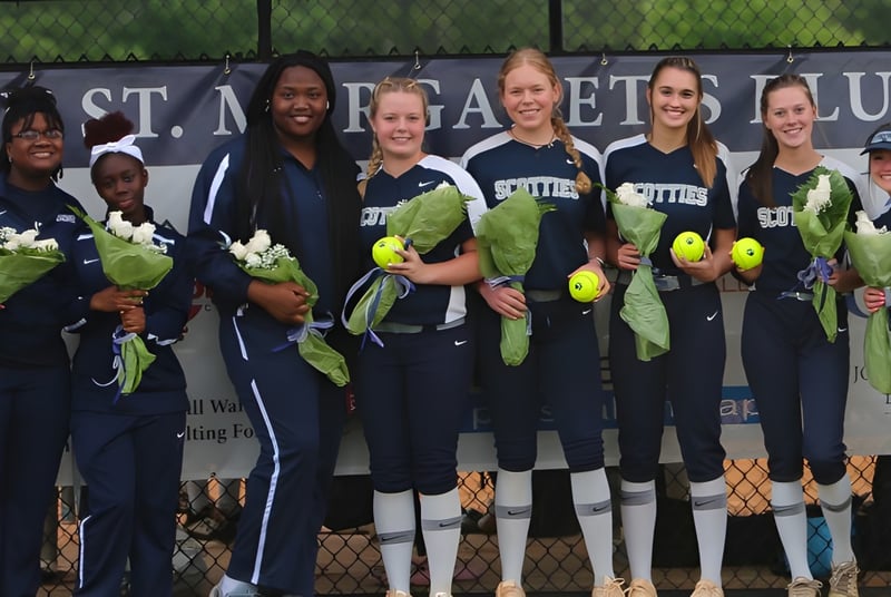 Un grupo de jugadoras de softball en uniforme está frente a una cerca con un banner de St. Margaret's School.