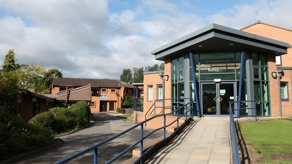 El moderno edificio de la St. Mary Catholic High School con arquitectura de vidrio y ladrillo y camino bajo un cielo nublado.