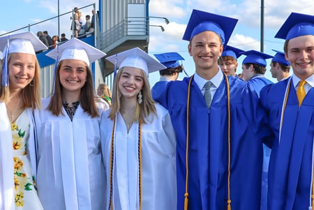 Un grupo de graduadas y graduados de la St. Mary Catholic High School está vestido de azul frente a un edificio escolar.