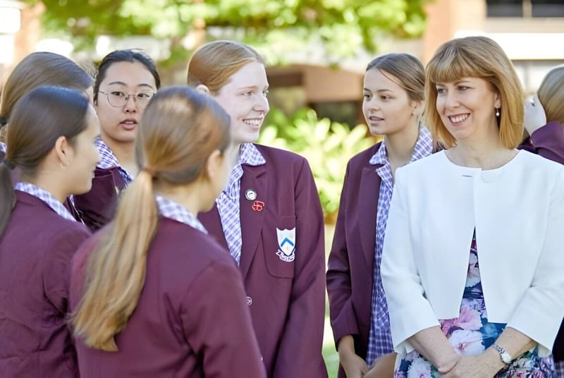 Un grupo de jóvenes estudiantes está en el campus de la St. Mary's Anglican Girls' School frente a árboles y edificios escolares.