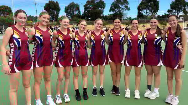 Un grupo de jóvenes deportistas está en camisetas rojas y azules juntos en el campo deportivo de la St. Mary's Anglican Girls' School.