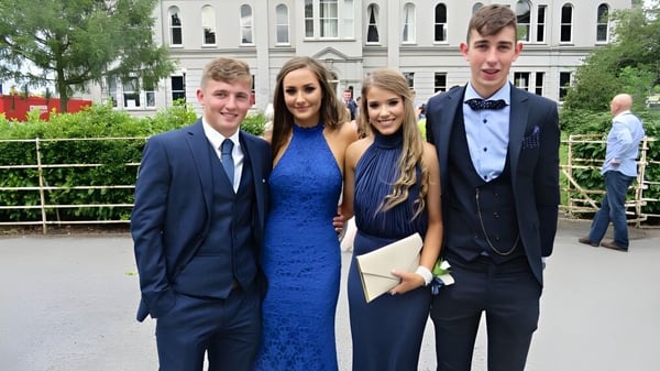 Cuatro estudiantes en ropa formal están de pie frente a un edificio histórico en el campus de St. Mary’s College.