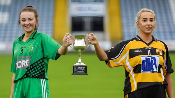 Dos alumnas de St. Mary's Holy Faith (Killester) sostienen juntas un trofeo en el campo deportivo.
