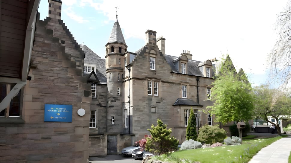 El histórico edificio de piedra de la St. Mary’s Music School está rodeado de plantas verdes y un camino pavimentado.
