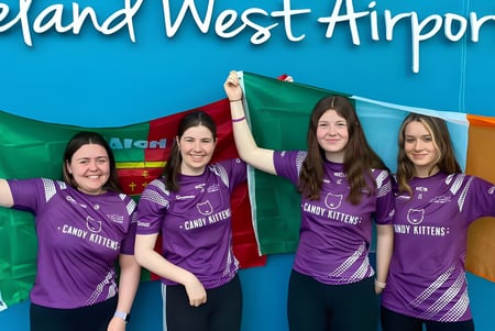 Cuatro alumnas de St. Mary’s Secondary están frente al cartel del Aeropuerto Ireland West con camisetas lila de Crazy Kittens.