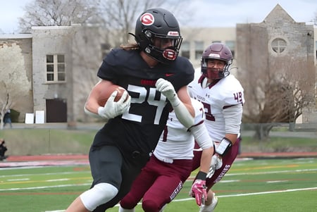Dos futbolistas juegan en el campo de deportes de la St. Matthew High School frente a edificios en el fondo.