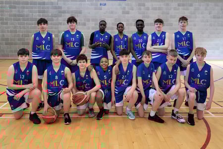 Un grupo de jóvenes jugadores y jugadoras de baloncesto posan en el gimnasio de St. Mel’s College frente a una pared de ladrillo.
