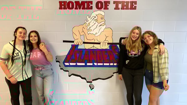 Cuatro estudiantes están frente al gran letrero con la inscripción Home of the Islanders en el terreno de St. Michael's Regional High.