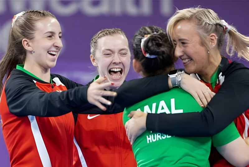 Tres alumnas en uniformes deportivos celebran y se abrazan en el campus de la St. Michael’s School frente a un fondo morado.