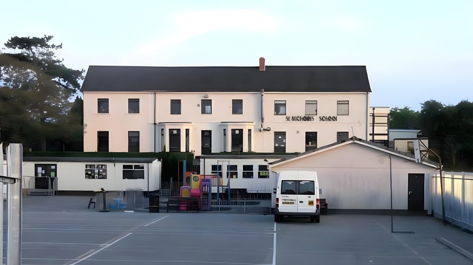 El edificio de varios pisos con techo negro y plaza en el terreno de la St. Michael’s School.