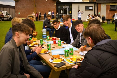 Un grupo de estudiantes del St. Mogues College disfruta de un picnic juntos en un campo al aire libre.