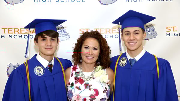 Tres estudiantes de la St. Mother Teresa High School llevan ropa de graduación frente a un fondo con la inscripción High School.