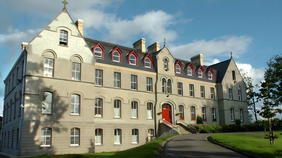 El edificio principal de varios pisos de St. Muredach's College está rodeado de vegetación verde.