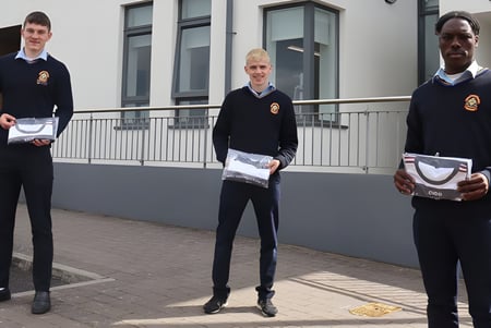 Tres alumnas y alumnos del St. Patrick's College están delante de un edificio gris con ventanas.