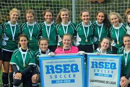 Las estudiantes de la St. Patrick’s High School posan con medallas frente a un banner de los RSEQ Soccer Champions de Ligue.