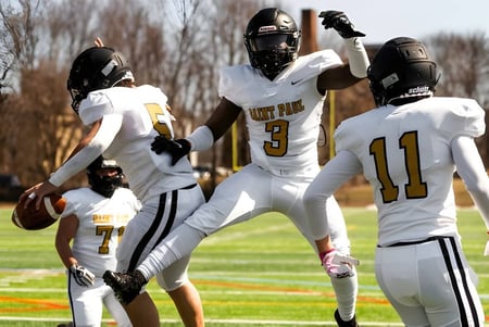 Un grupo de jugadores de fútbol americano con camisetas blancas juega en el campo deportivo de la St. Paul Catholic High School.