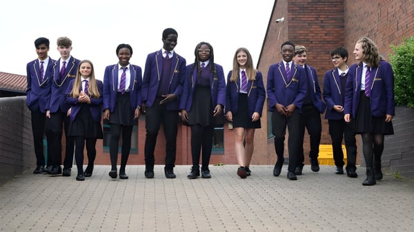 Un grupo de alumnos en uniformes escolares está frente a un edificio de ladrillo en el terreno de la St. Paul Catholic High School.