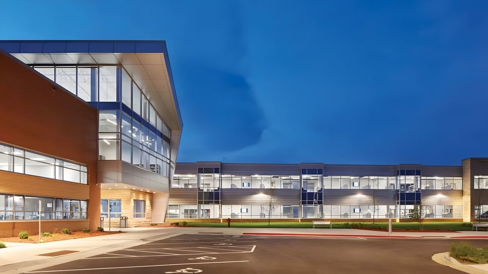 El moderno edificio de varios pisos de la St. Peter High School con grandes ventanales de vidrio y fachada naranja se encuentra bajo un cielo azul claro.