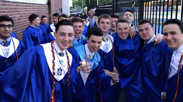 Un grupo de estudiantes de la St. Peter High School está en túnicas de graduación azules frente a un edificio de ladrillo y posan para una foto.