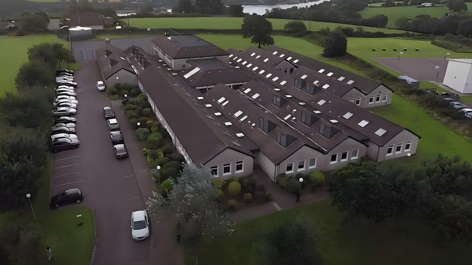 El edificio escolar de St. Peter's Community School está rodeado de áreas verdes y una calle con coches estacionados.