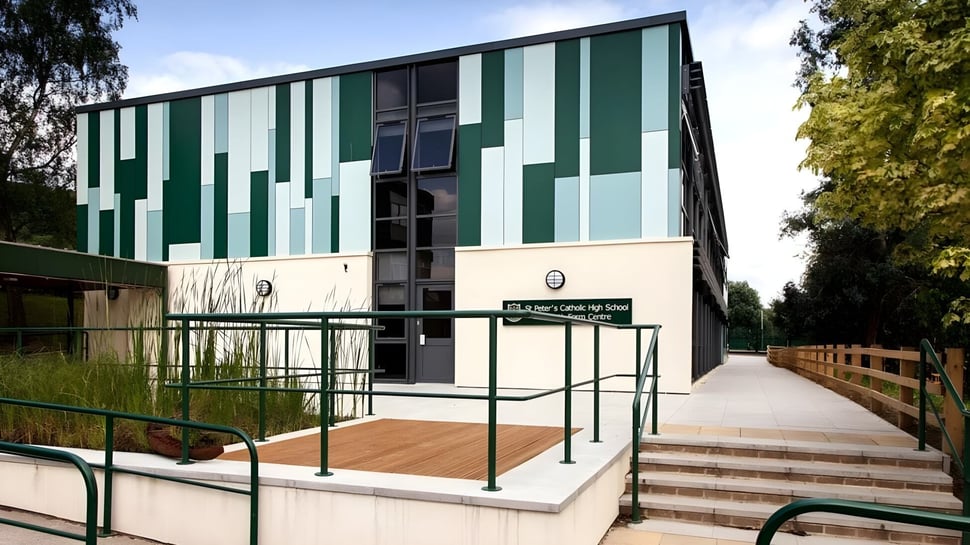 El moderno edificio de varios pisos con fachada verde y blanca de la St. Peter’s High School se encuentra en un entorno rodeado de árboles.
