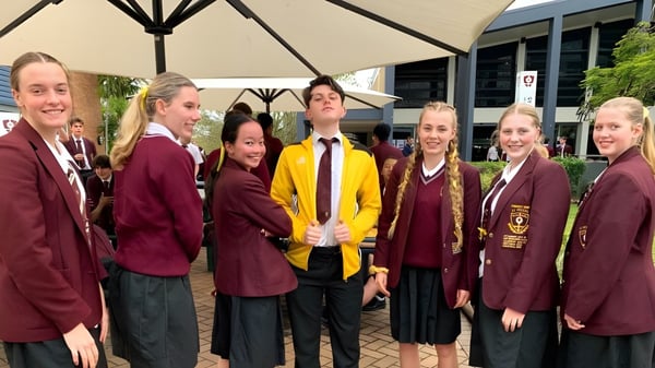 Un grupo de estudiantes en St. Peters Lutheran College está afuera reunido bajo una gran sombrilla.