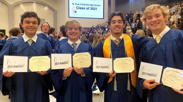 Cuatro egresados de la St. Pius X High School en togas sostienen sus diplomas en una ceremonia de graduación.