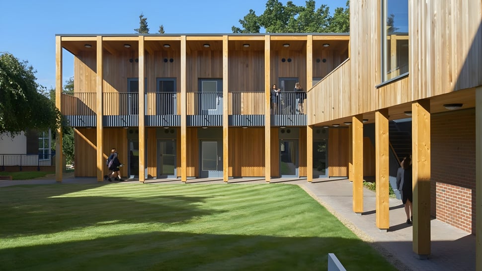 El moderno edificio de madera con grandes ventanas y un patio verde en el campus de St. Teresa’s College.