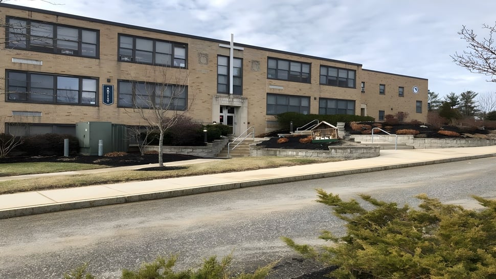 El edificio de ladrillo de varios pisos de la St. Thomas Aquinas High School con grandes ventanas en una calle arbolada.