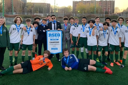 Un grupo de estudiantes de la St. Thomas High School celebra la victoria en el campo de fútbol con trofeo y medallas frente al paisaje urbano.