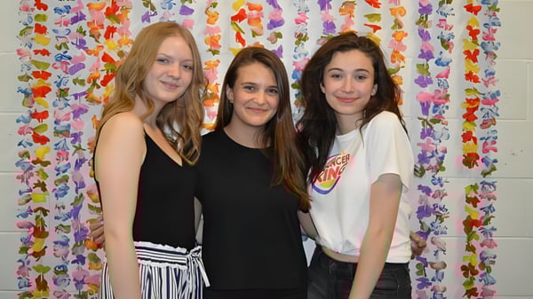 Tres estudiantes de la St. Thomas High School están frente a un colorido telón de flores.