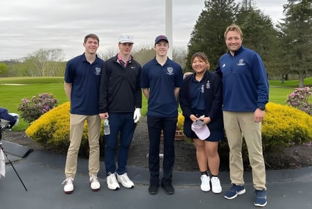 Un grupo de estudiantes de la St. Thomas More School está juntos en el parque con árboles y áreas verdes de fondo.