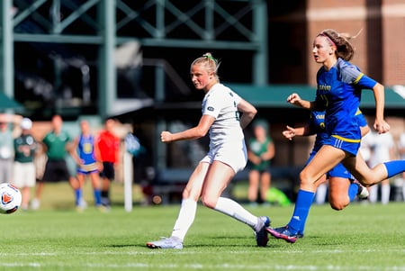 Estudiantes juegan un partido de fútbol en el campo deportivo de la St. Tiernan’s Community School con espectadores al fondo.