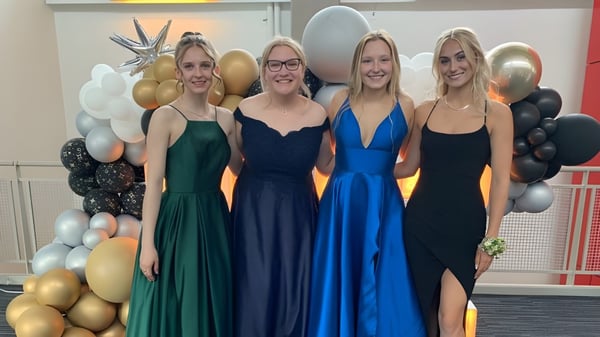 Cuatro estudiantes de la St. Timothy High School posan frente a un fondo de globos de colores.