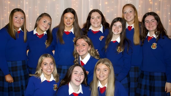Un grupo de estudiantes en uniformes azules con acentos rojos posan frente a un fondo brillante en el campus de la St. Vincent's Secondary School.
