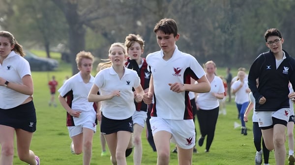 Un grupo de estudiantes de Stamford High School corre juntos en el campo de deportes entre los árboles.