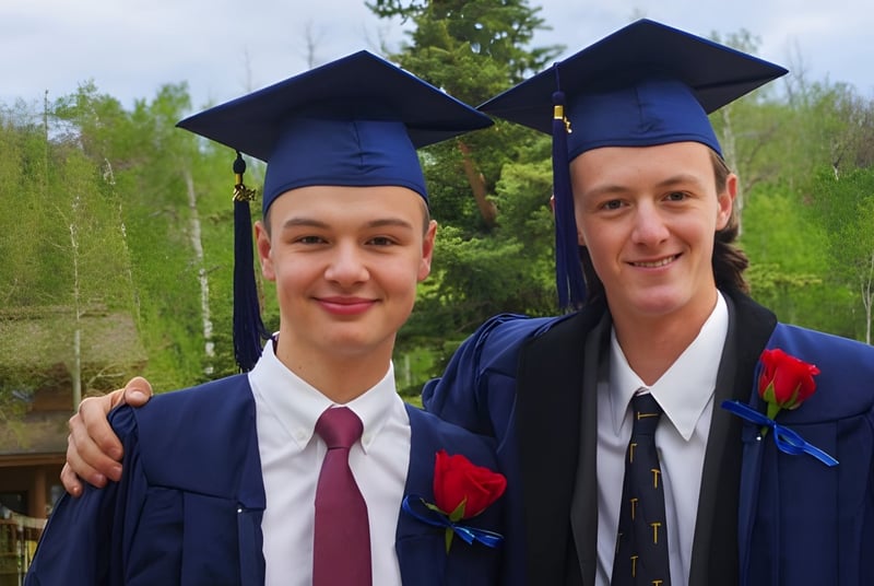 Dos estudiantes de la Steamboat Mountain School están juntos al aire libre en sus togas de graduación.